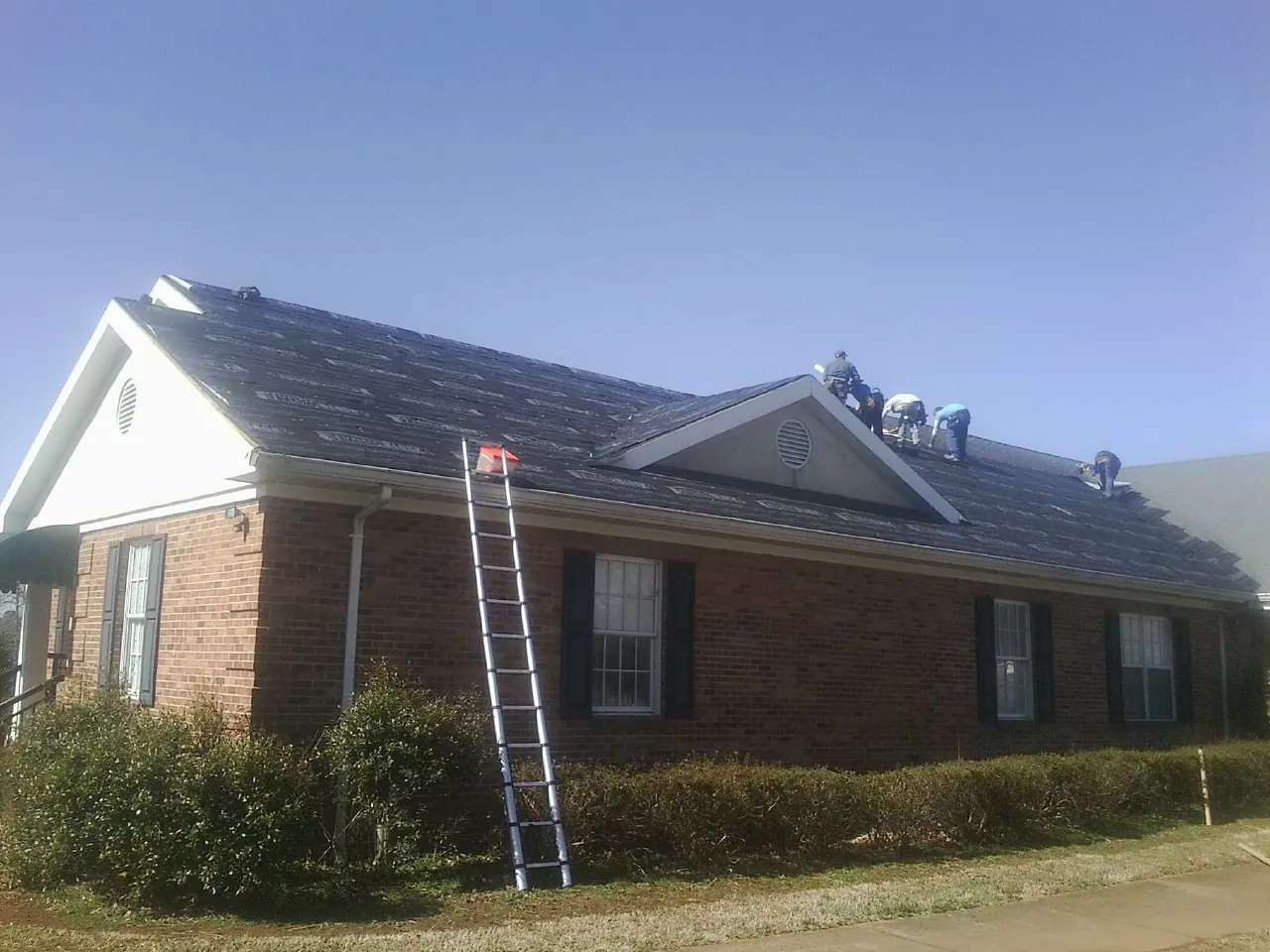 Crew tearing shingles off a brick ranch roof with a ladder set — Emergency Roof Repair work by our crew in Herrick