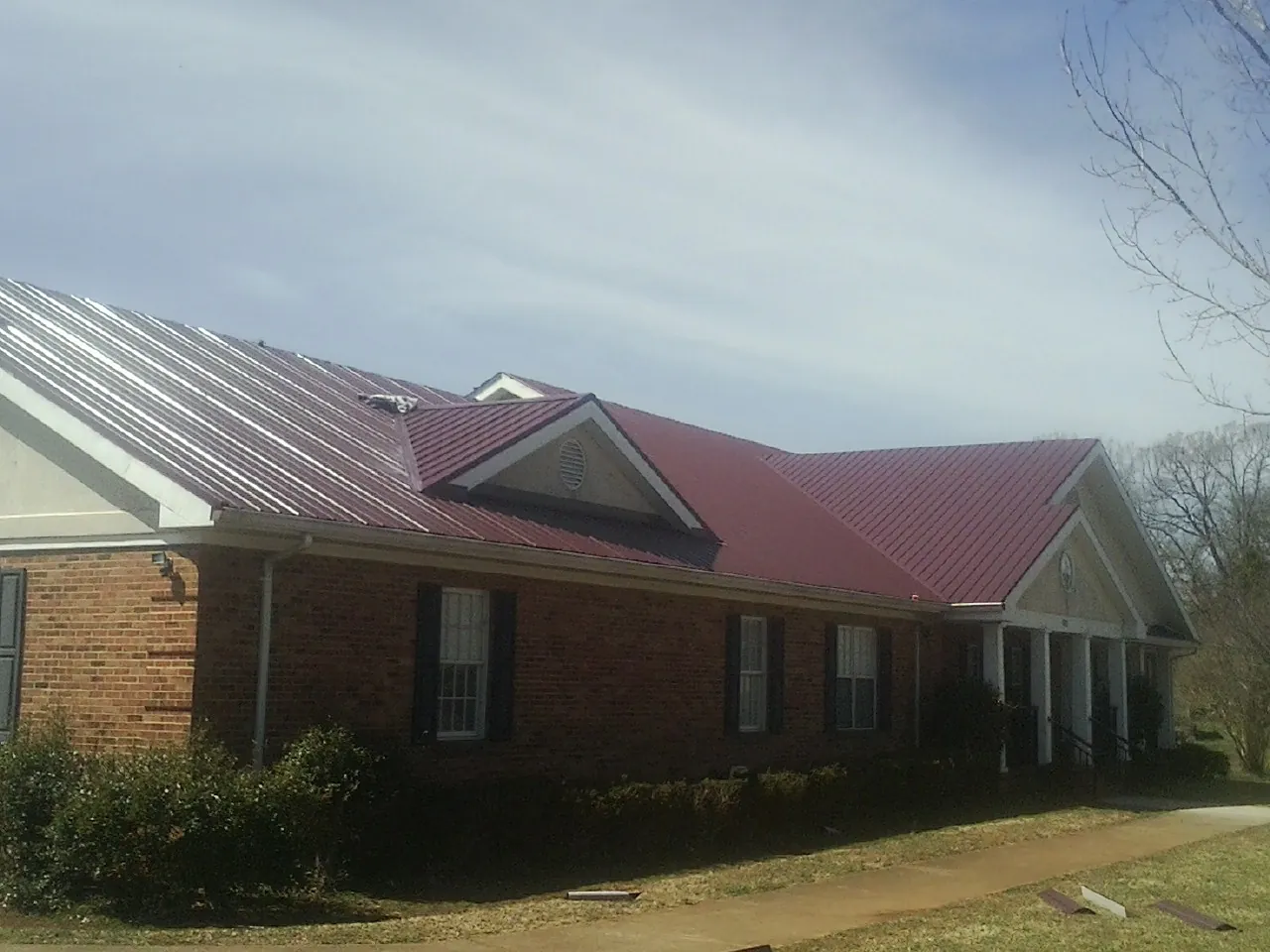 Red metal roof with gabled entries on a long brick building, from a Hail Damage Roof Repair job in Herrick