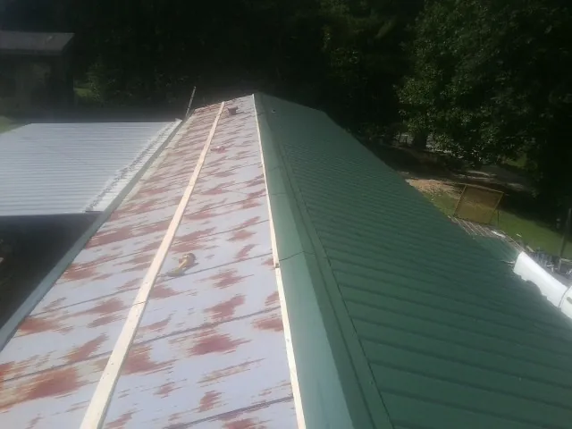 Old rusted panels beside newly installed green metal roofing — Wind Damage Roof Repair by Roofing Brothers in Herrick