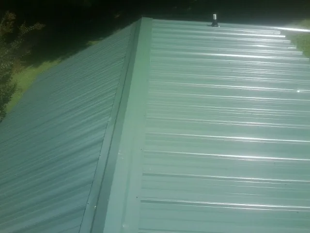 New green metal panels meeting at the ridge of a roof — Flat Roof Repair work by our crew in Herrick