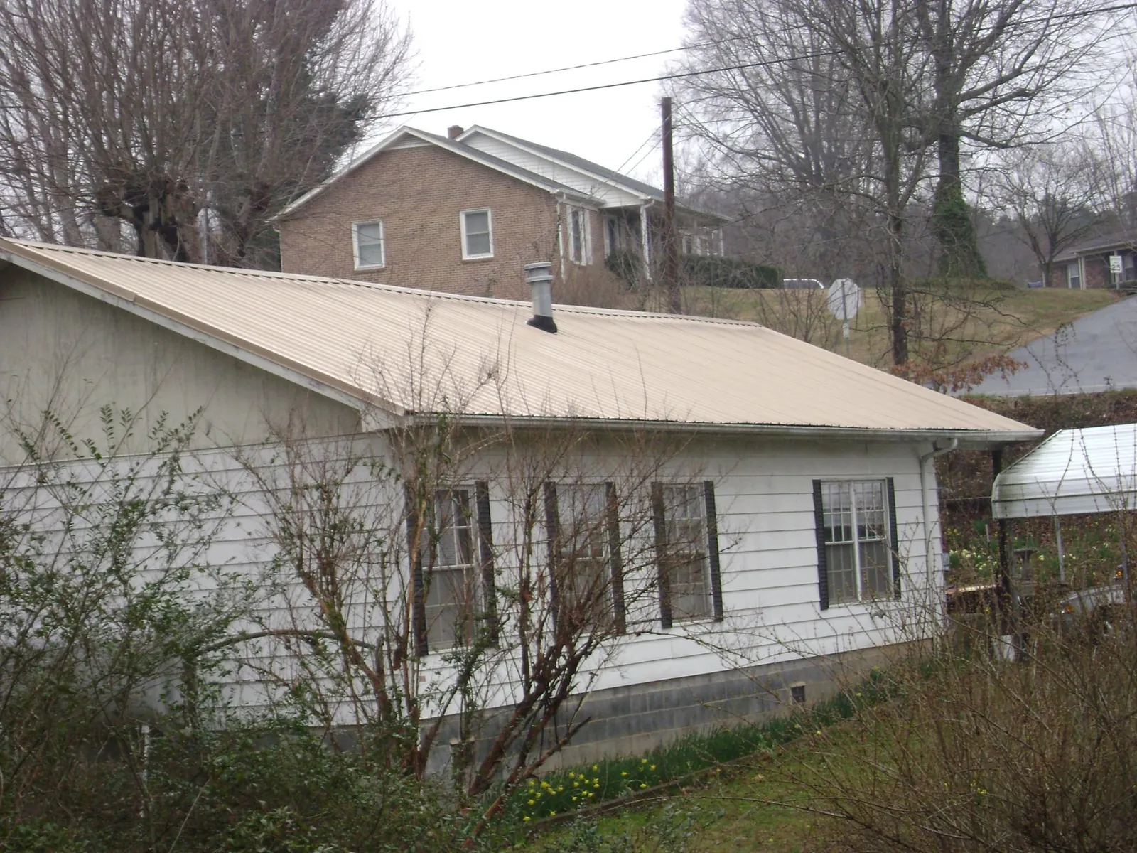 Tan metal roof on a white sided house set into a hillside — Commercial Roofing by Roofing Brothers in Herrick
